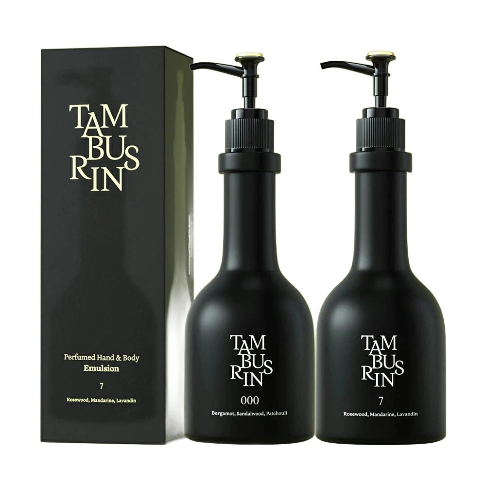 
The image shows a set of TAMBUSI hand and body emulsion products. There are two black bottles with pumps labeled "000" and "7". The bottles are placed next to a black rectangular box with the brand name "TAMBUSI" written in gold lettering on it.